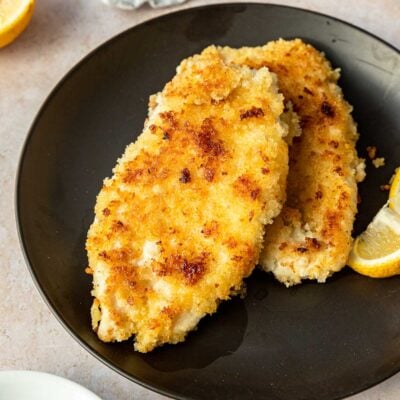 Cooked Chicken Schnitzel on a black plate with lemon wedge.