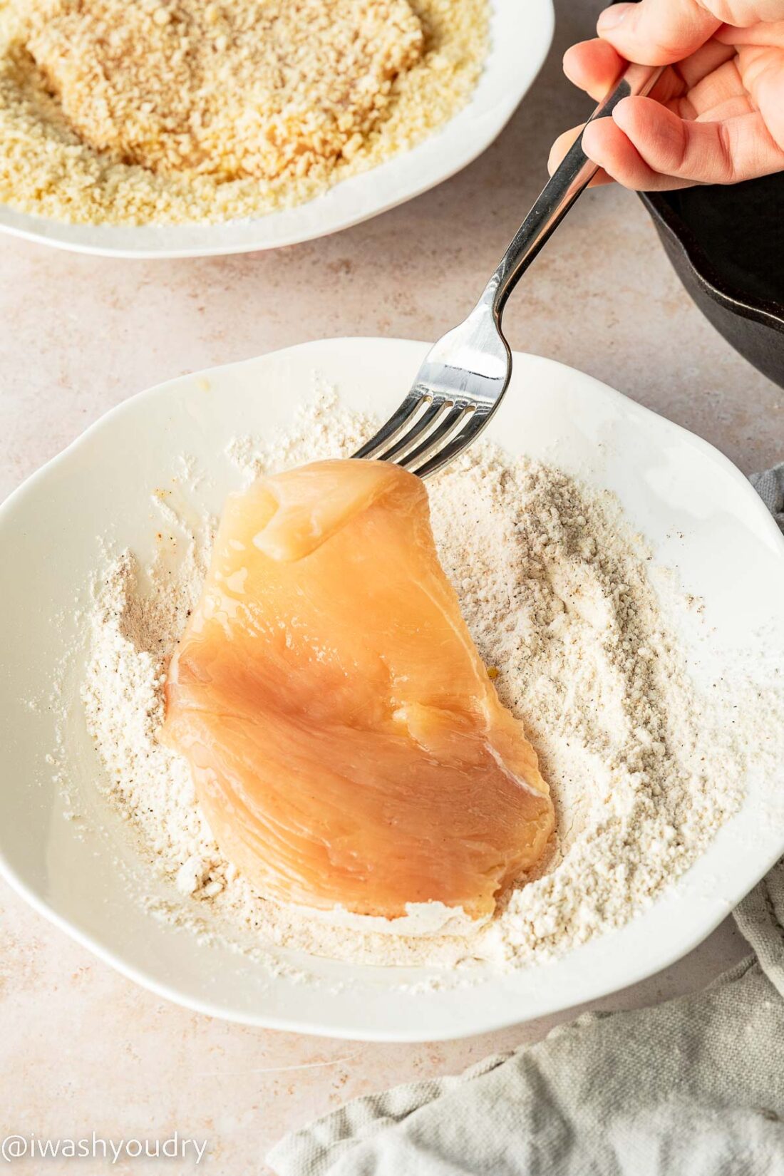 Raw chicken on fork dipping into white bowl of flour. 