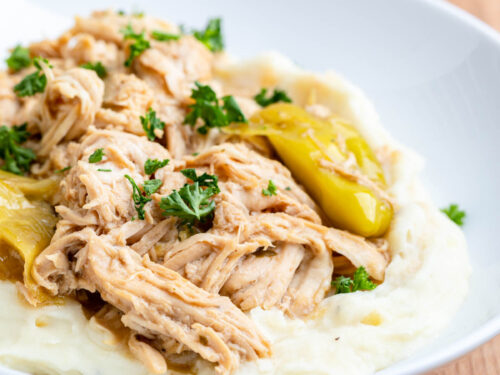 Cookied Slow Cooker Mississippi Chicken on mashed potatoes on white plate.