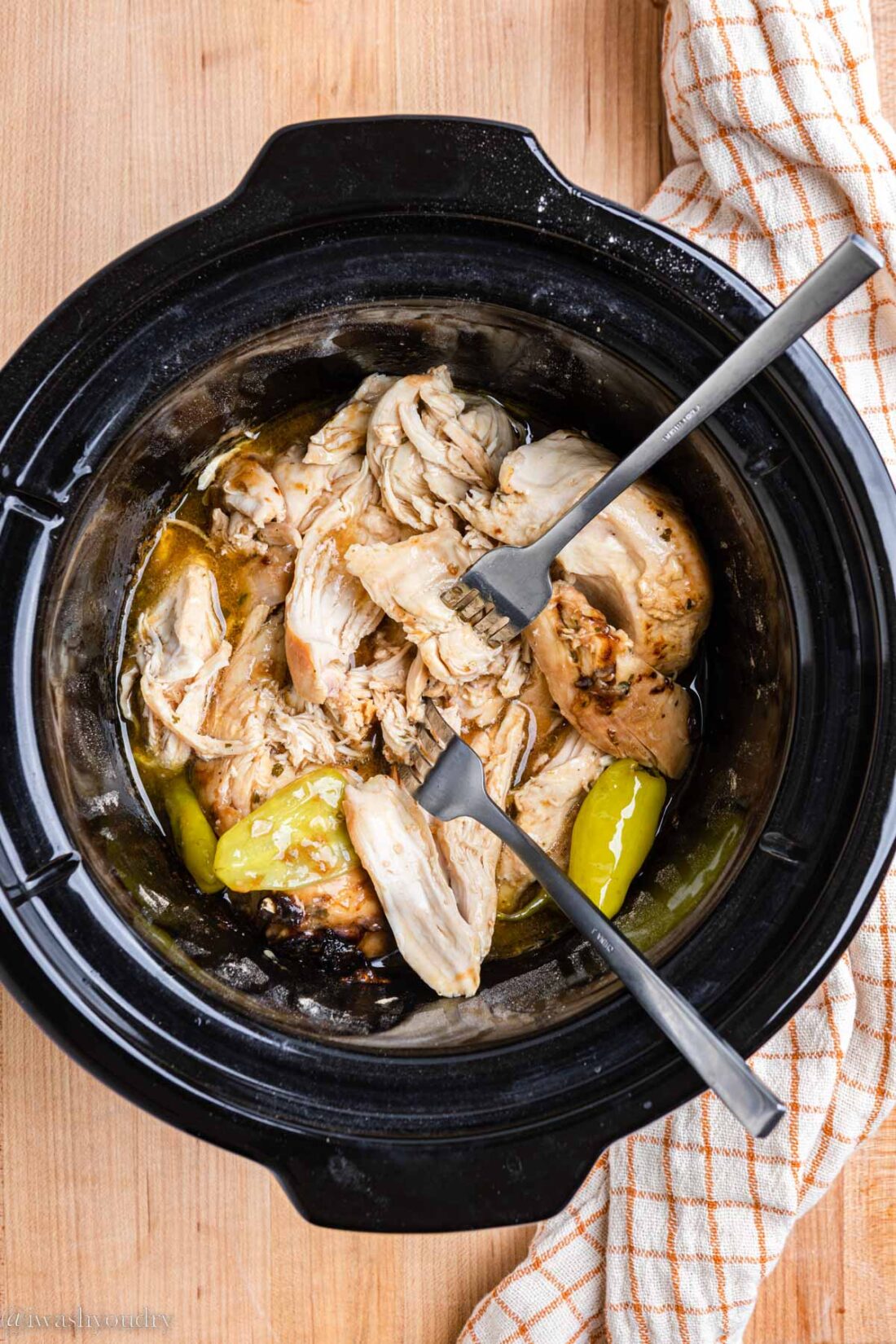 Two forks shredding slow cooker mississippi chicken in black crock pot. 
