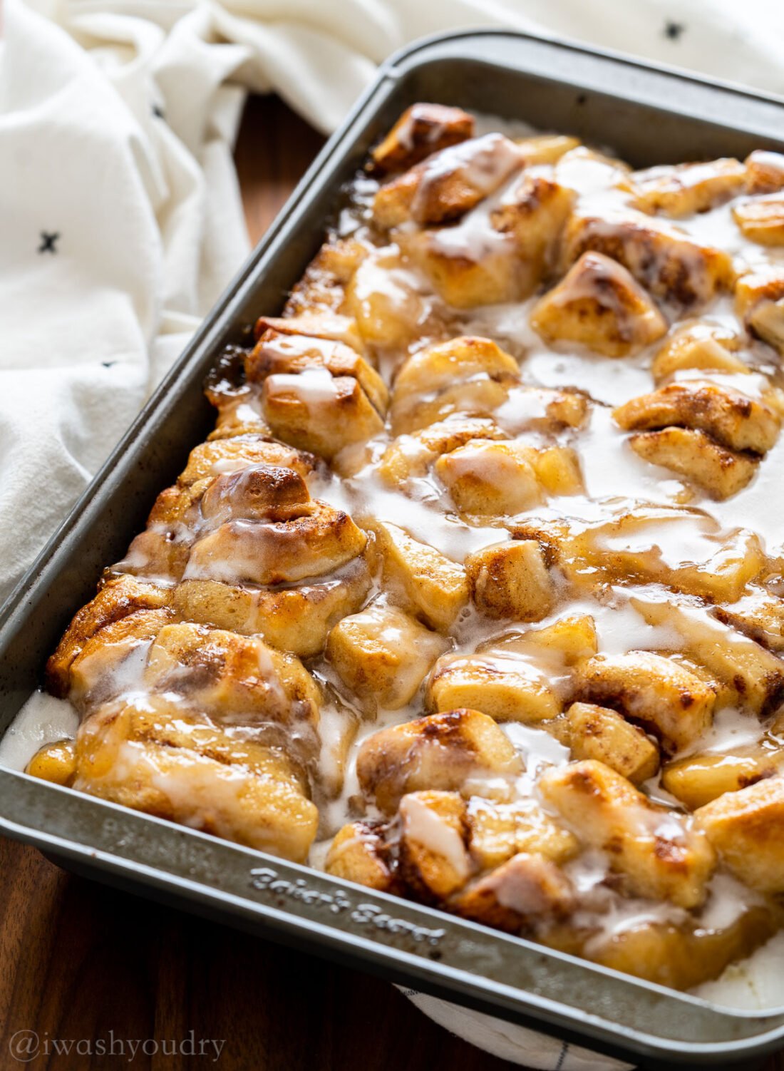 Baking dish with cinnamon rolls and apples with white frosting on top.
