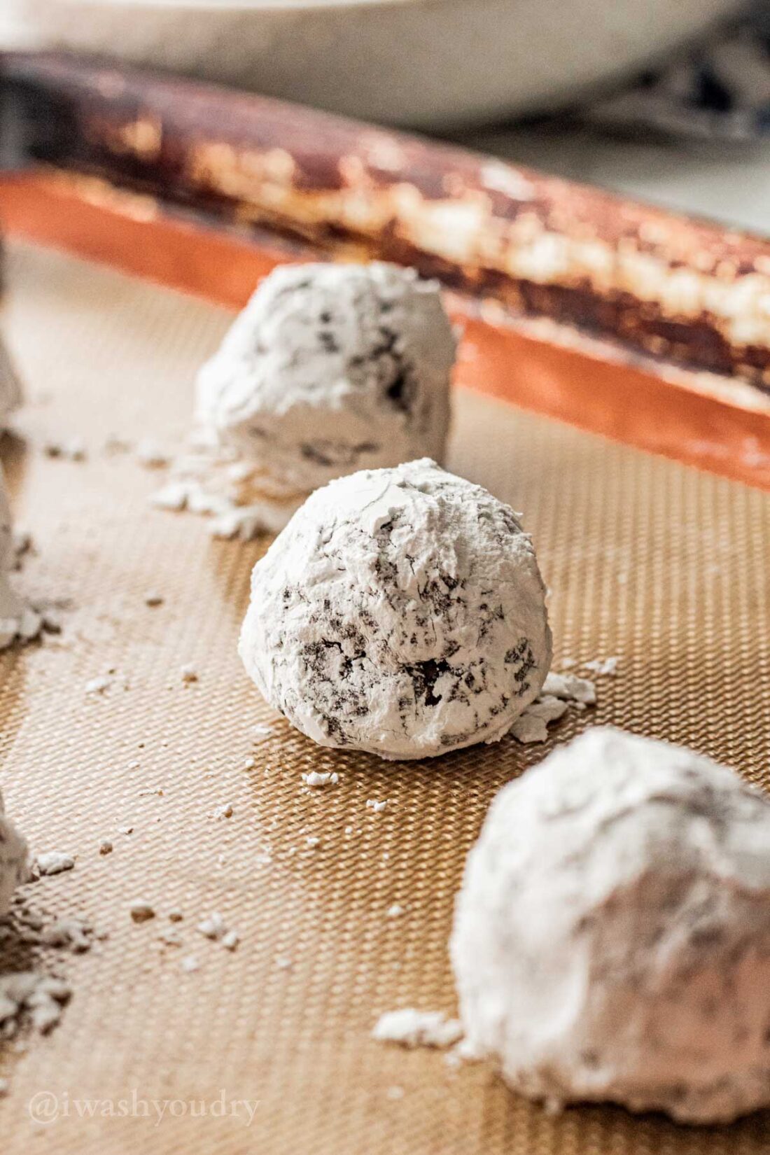 Raw chocolate crinkle cookies rolled in powdered sugar on metal pan. 