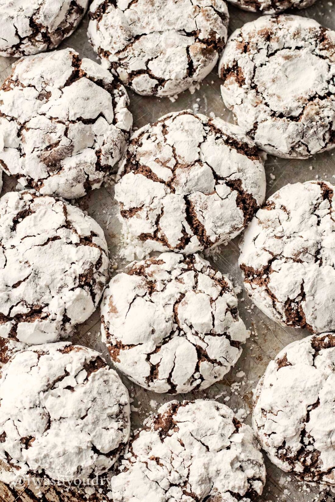 Baked chocolate crinkle cookies grouped together on metal pan.