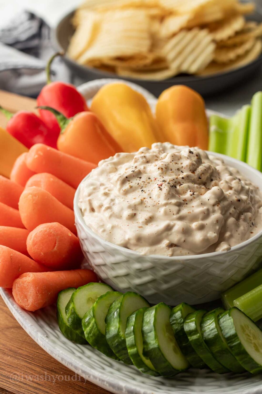 chip dip in white bowl with veggies around it.