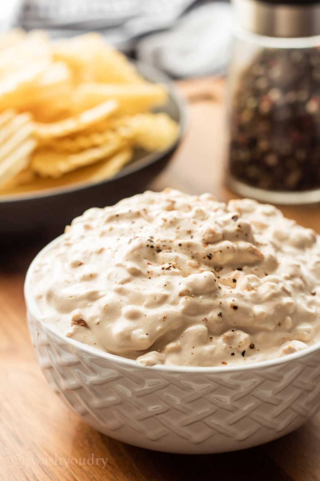 chip dip in white bowl with chips in back. 