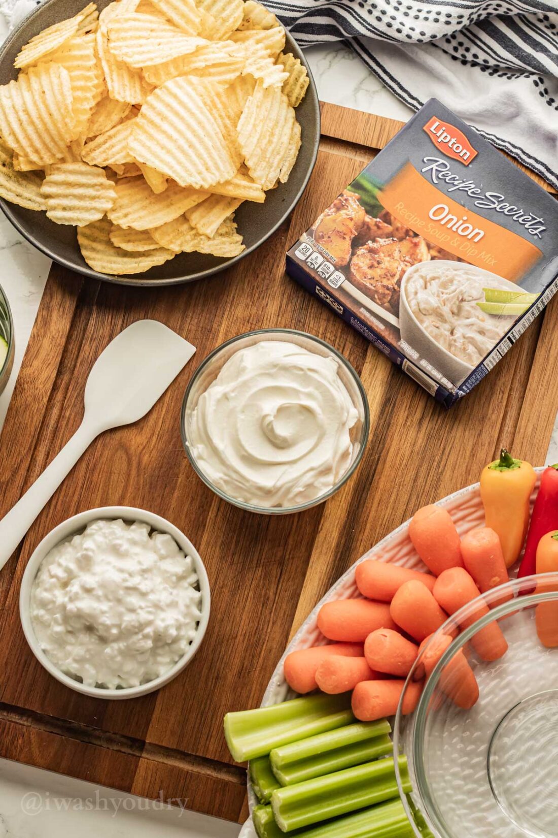 ingredients for creamy onion dip on wooden surface with chips and veggies.