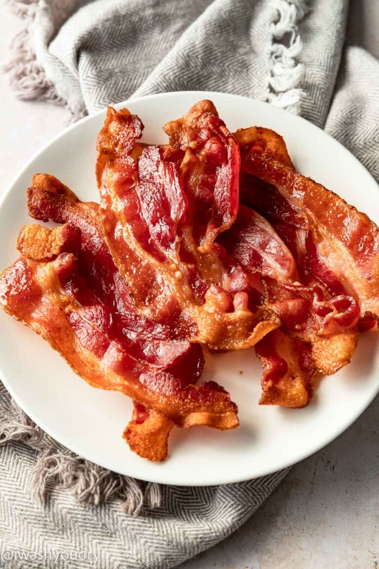 Cooked bacon slices on white plate with dish towel.