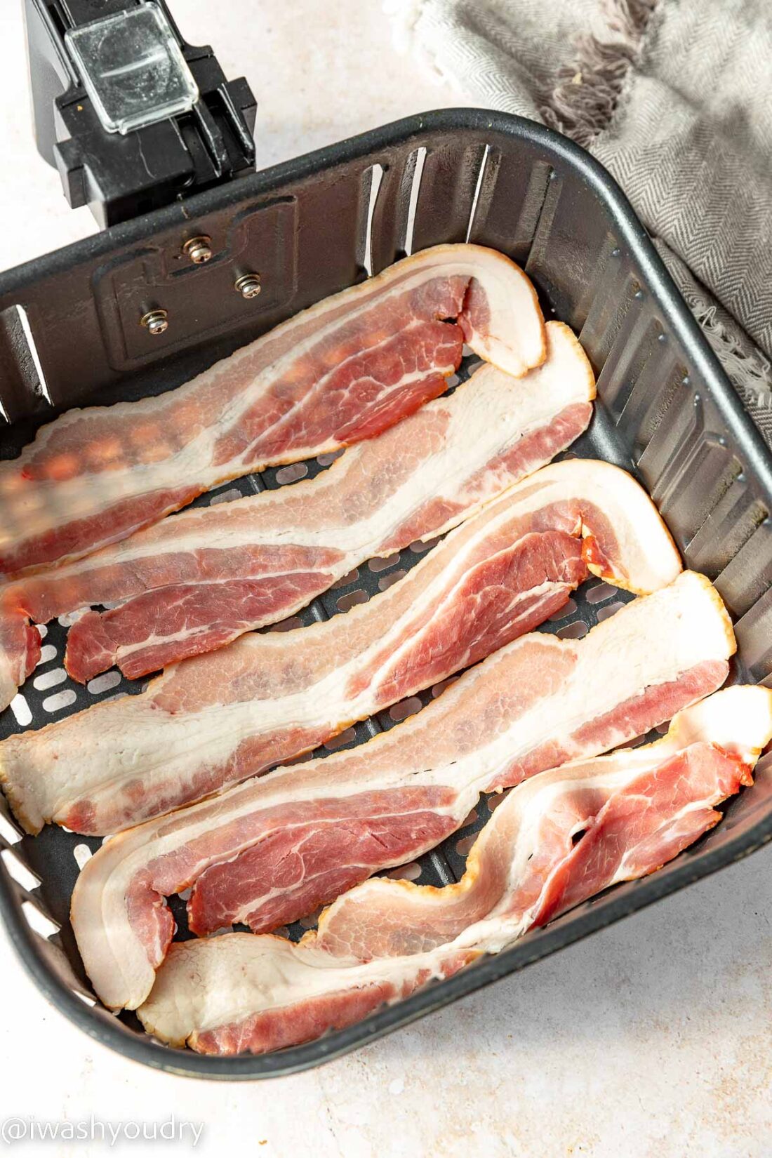 Raw bacon in single layer in air fryer basket. 