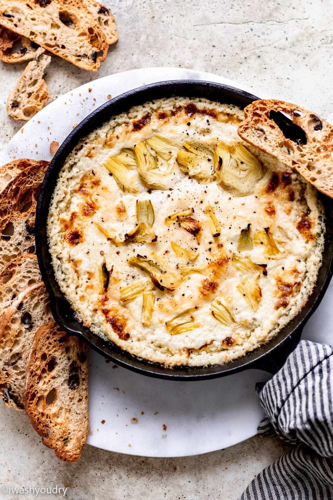 Hot Artichoke Dip in black bowl with slices of bread around.