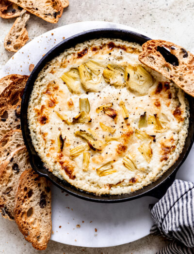 Hot Artichoke Dip in black bowl with slices of bread around.
