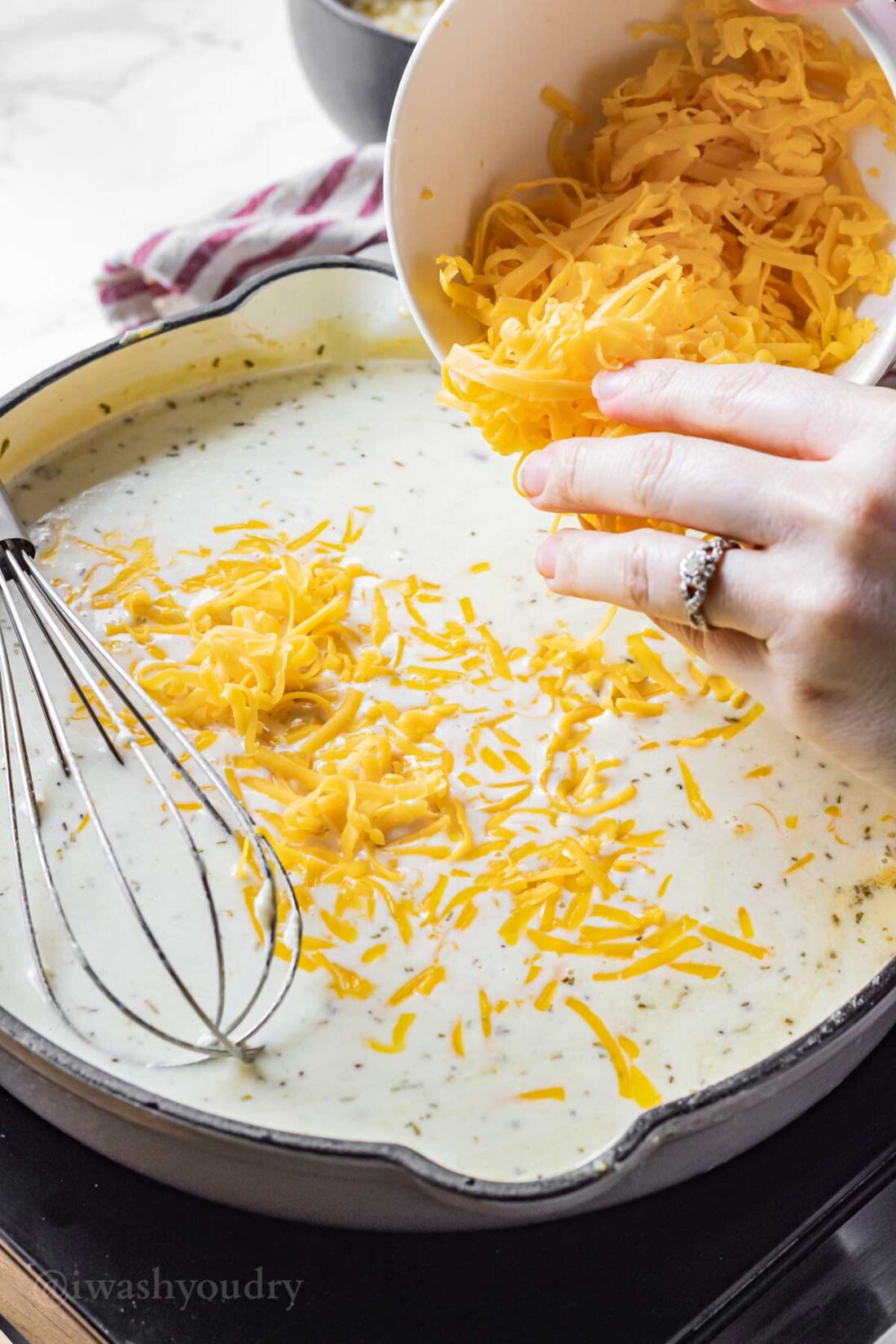 Hands sprinkling cheese into frying pan of sauce with whisk. 