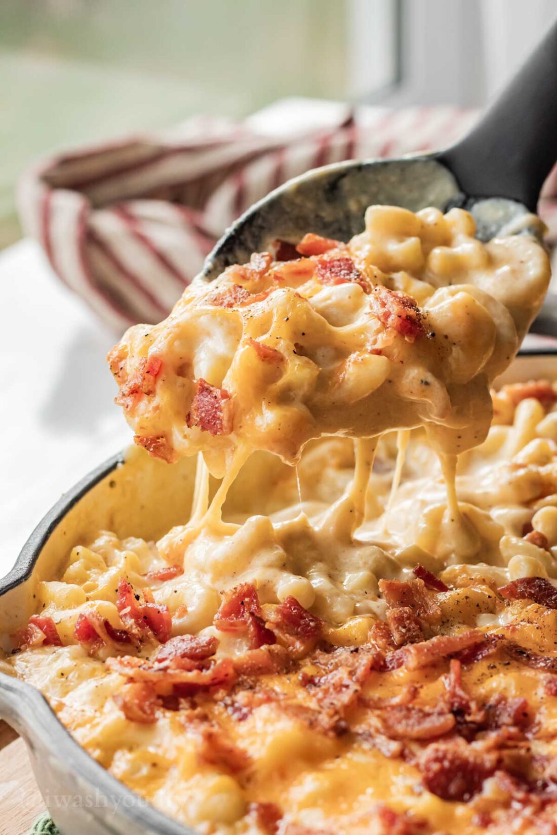 Spoonful of melty baked bacon mac and cheese above skillet. 