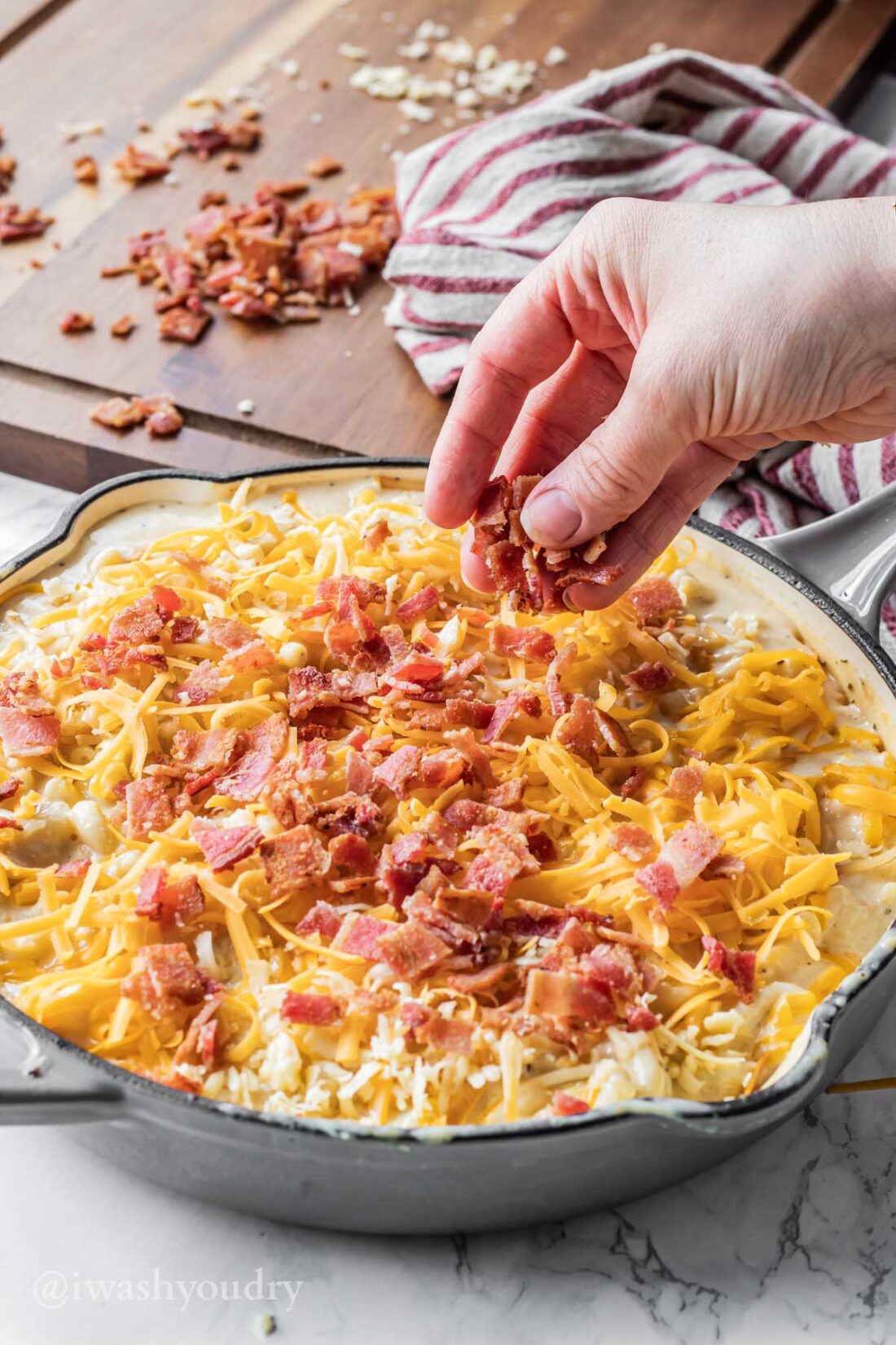 Hand sprinkling bacon over unbaked mac and cheese in skillet. 