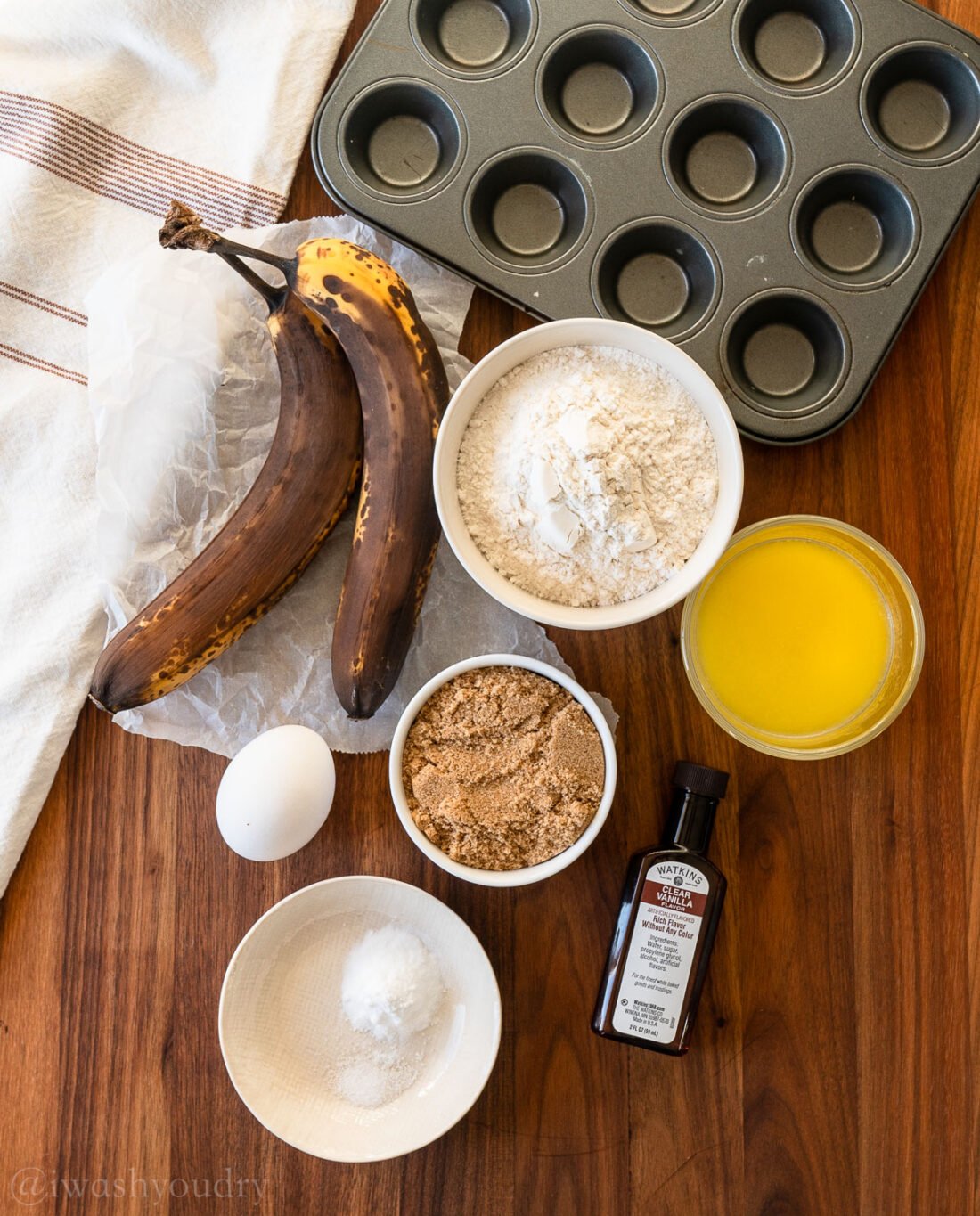 Ingredients for banana muffins on wooden surface with muffin tin.