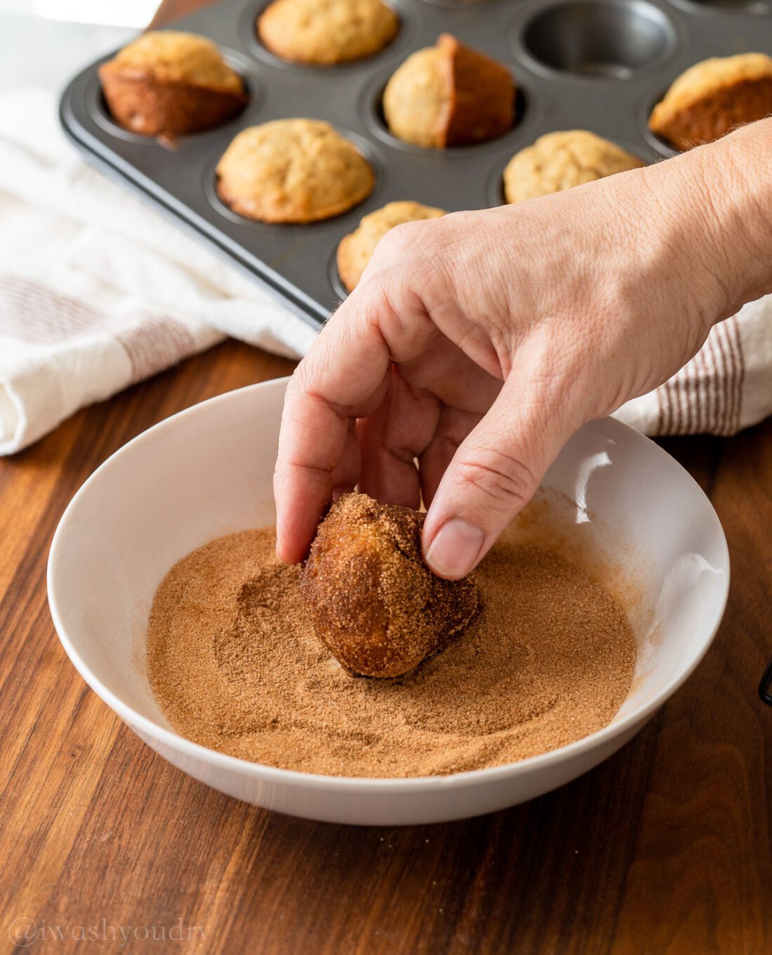 rolling muffins in cinnamon and sugar mixture in white bowl.