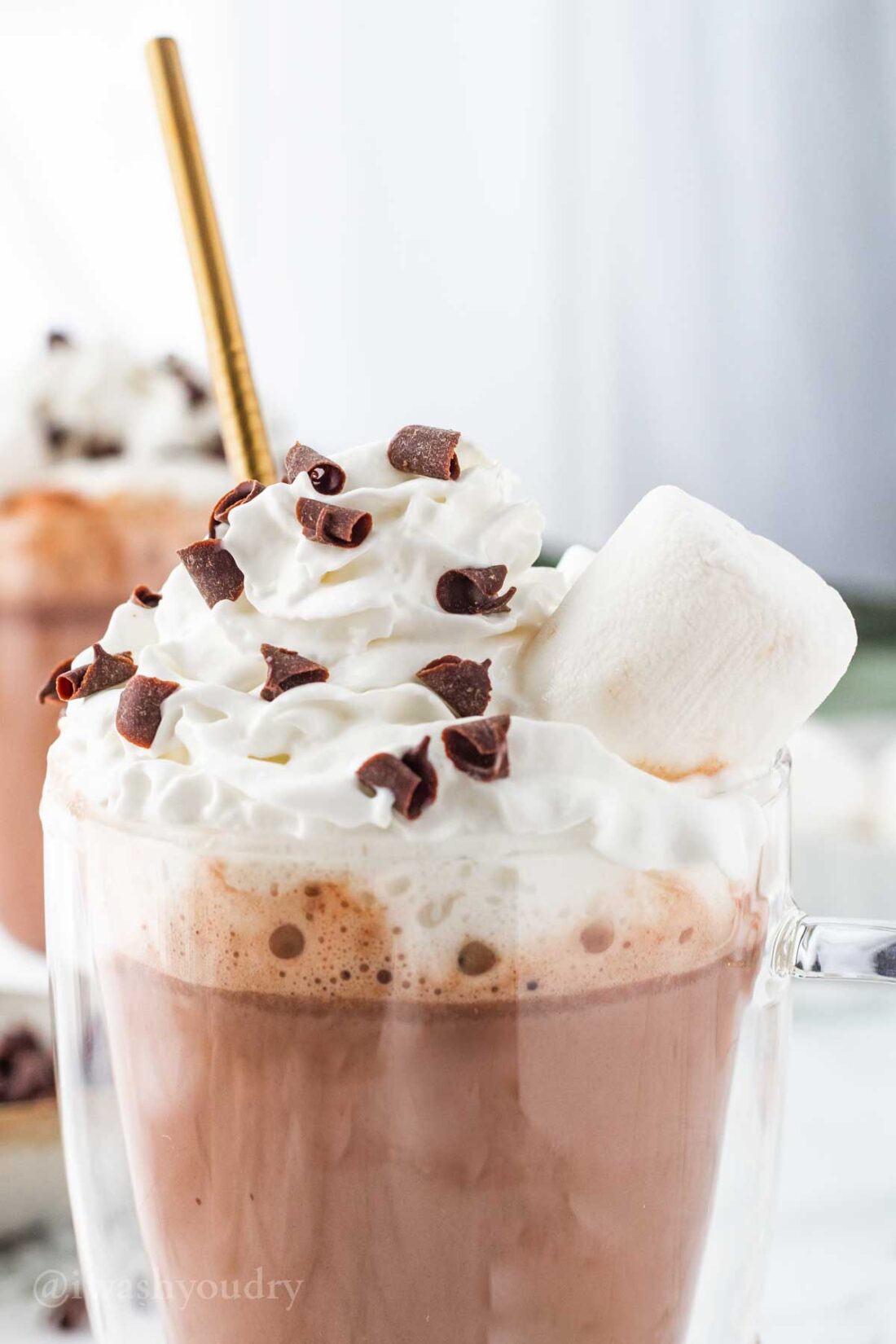 Glass mug of hot chocolate with whipped cream and marshmallow on top. 