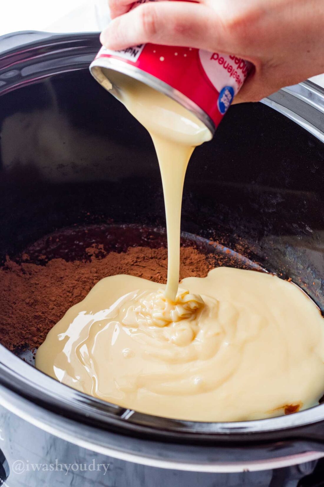 Pouring sweet condensed milk into crock pot with cocoa powder. 
