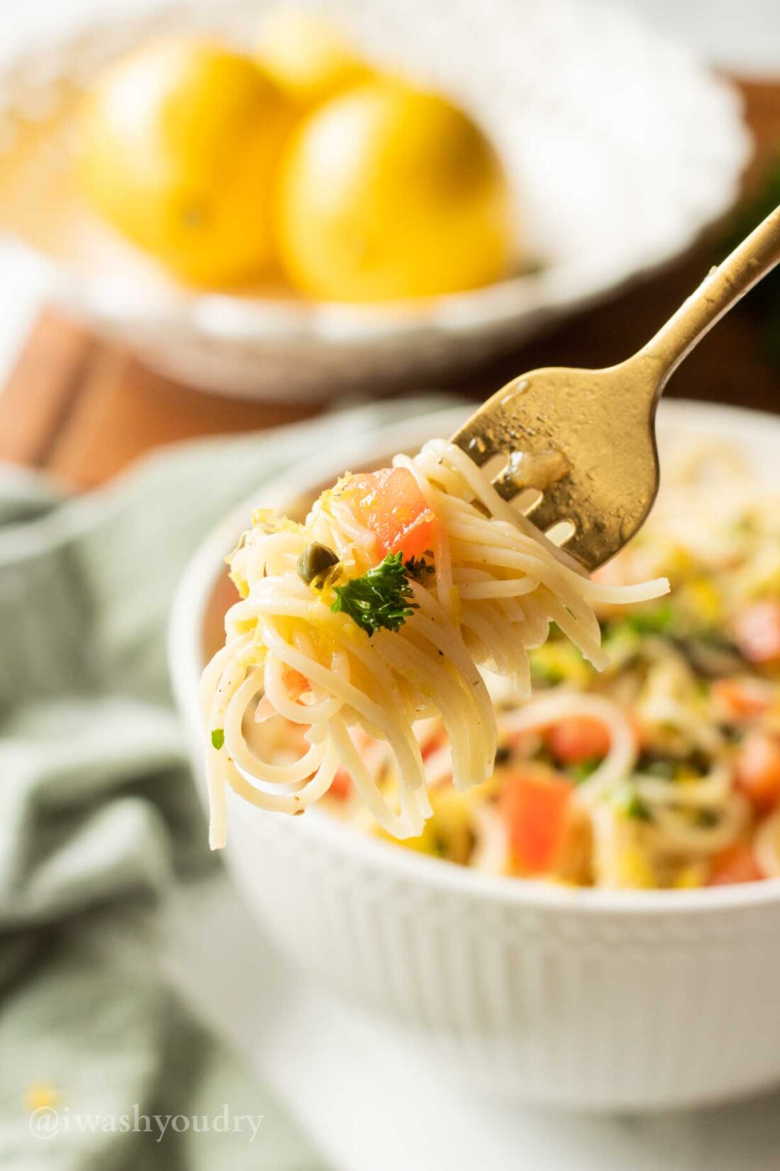 Forkfull of lemon capellini pasta salad above white bowl of pasta. 