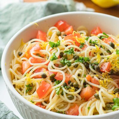 Lemon Capellini salad in white bowl with green dish towel and lemons.