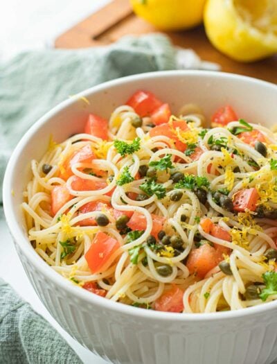 Lemon Capellini salad in white bowl with green dish towel and lemons.