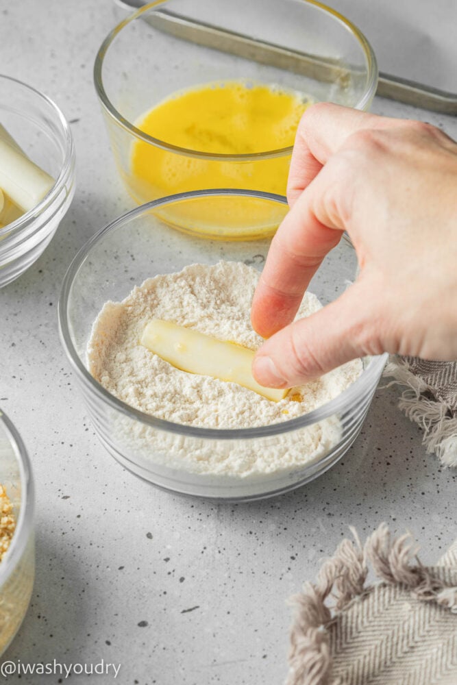 Dipping cheese stick into bowl with flour.