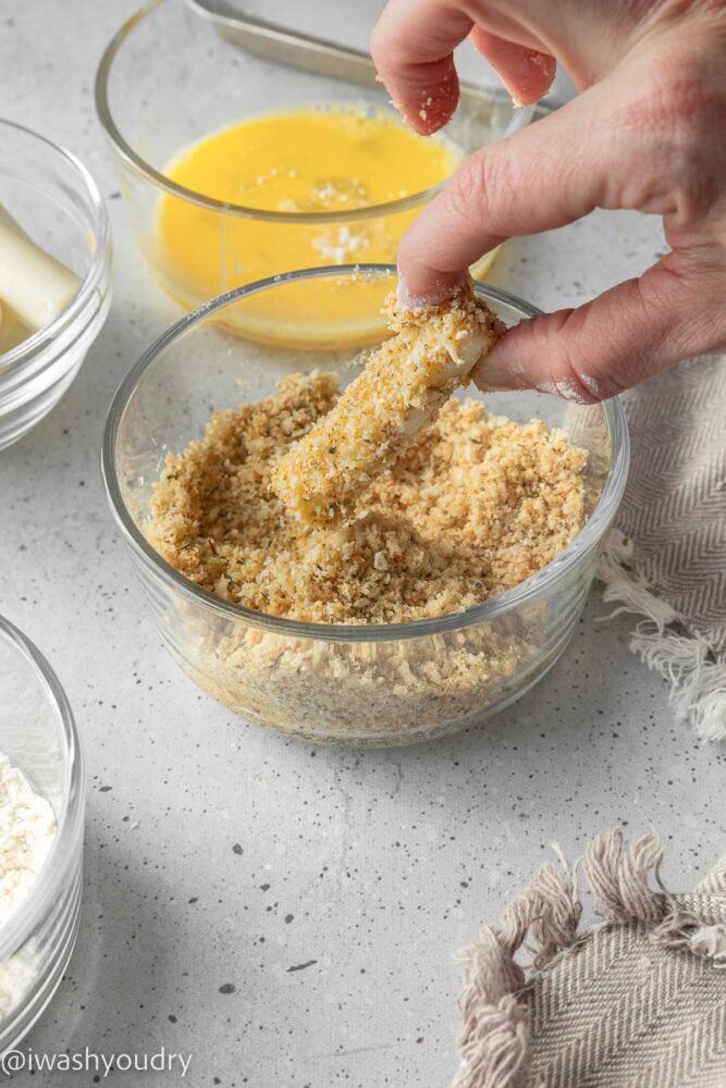 bread coated cheese stick in glass bowl with right hand.