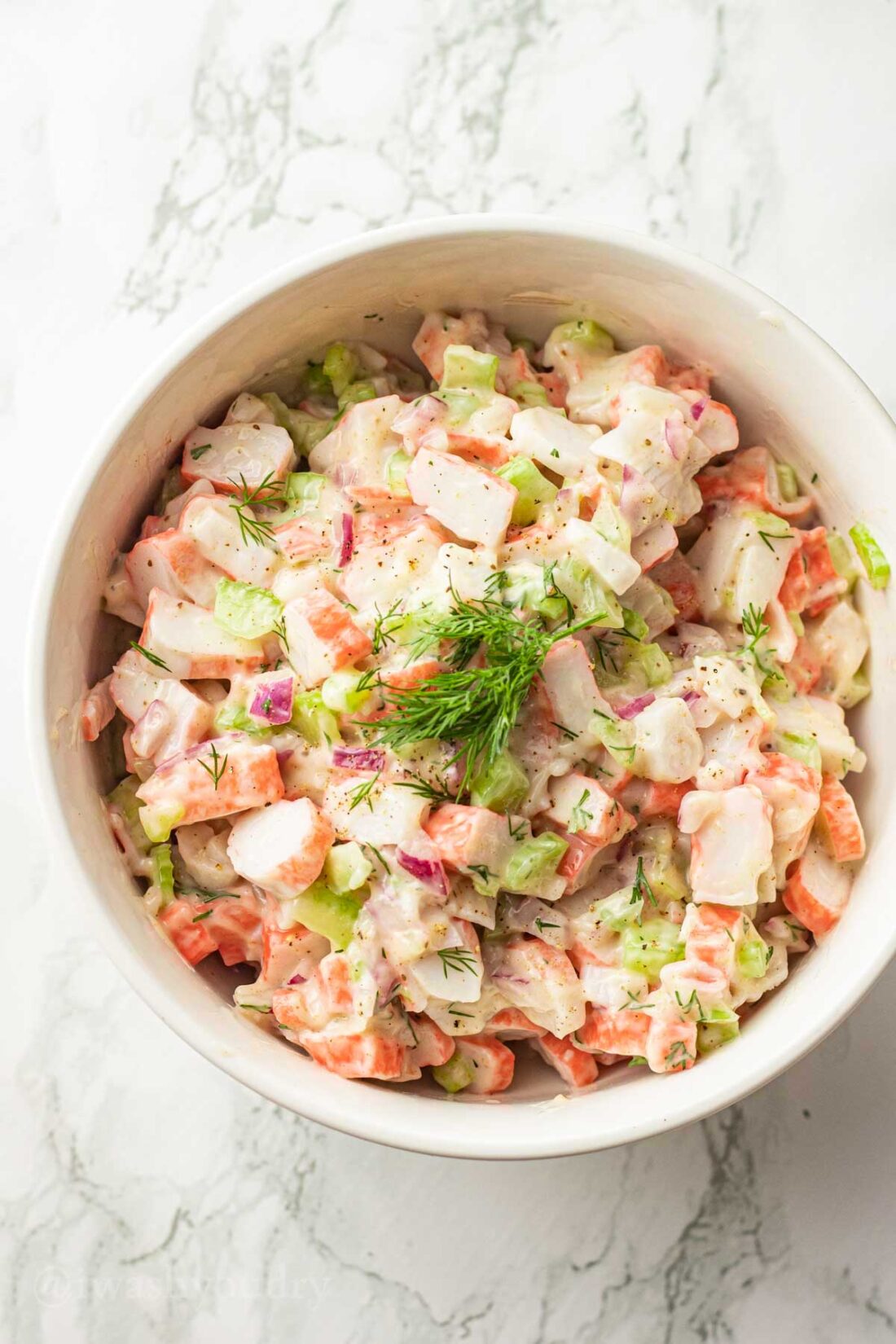 bowl of creamy cold crab salad with fresh dill on top.