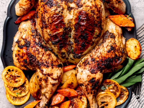 Whole roasted spatchcock chicken on platter with vegetables.
