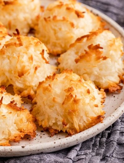 Baked coconut macaroon cookies on white plate over dish towel.