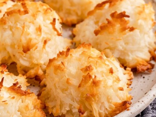 Baked coconut macaroon cookies on white plate over dish towel.