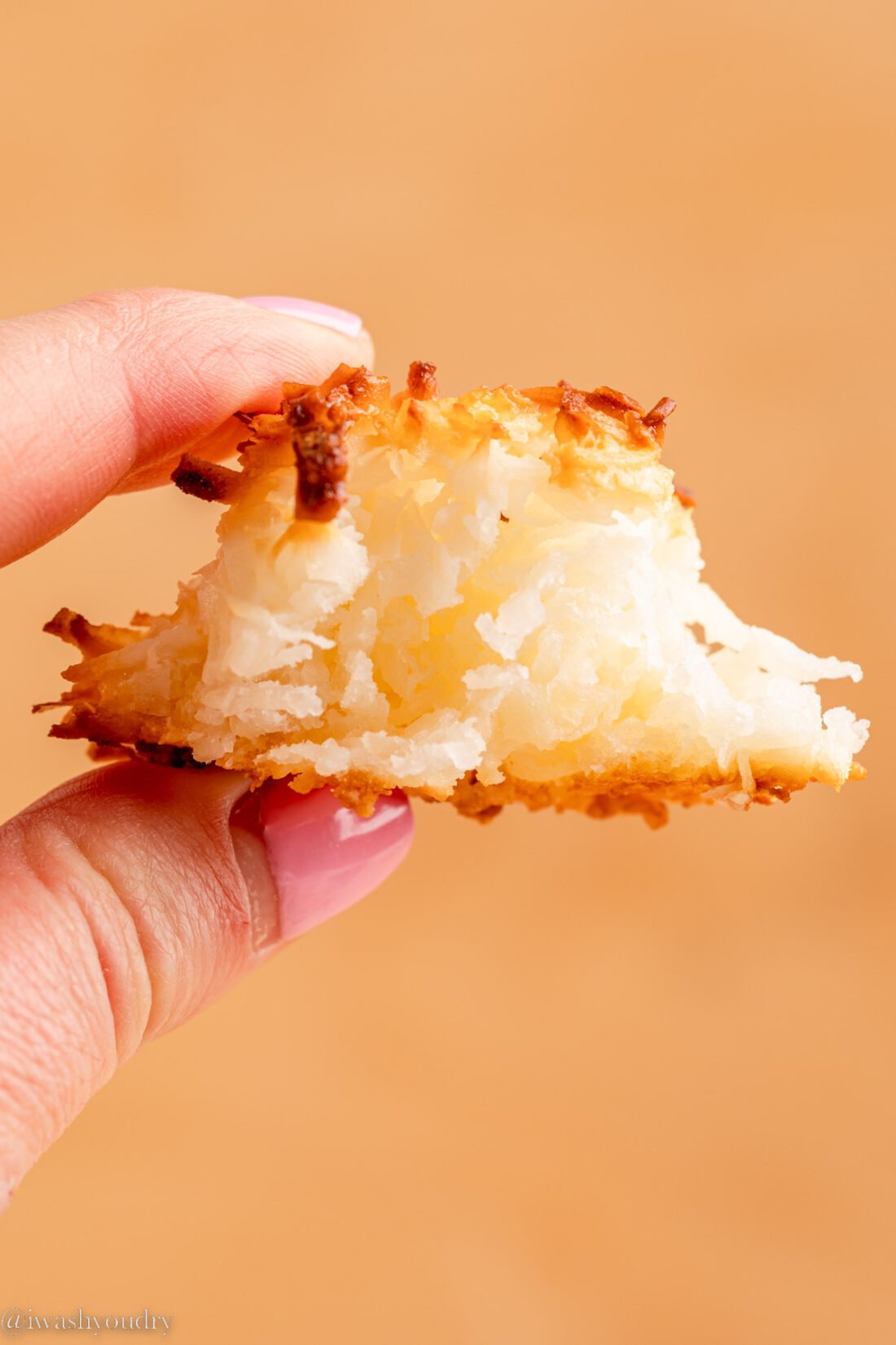 Hand holding half of a coconut macaroon cookie. 