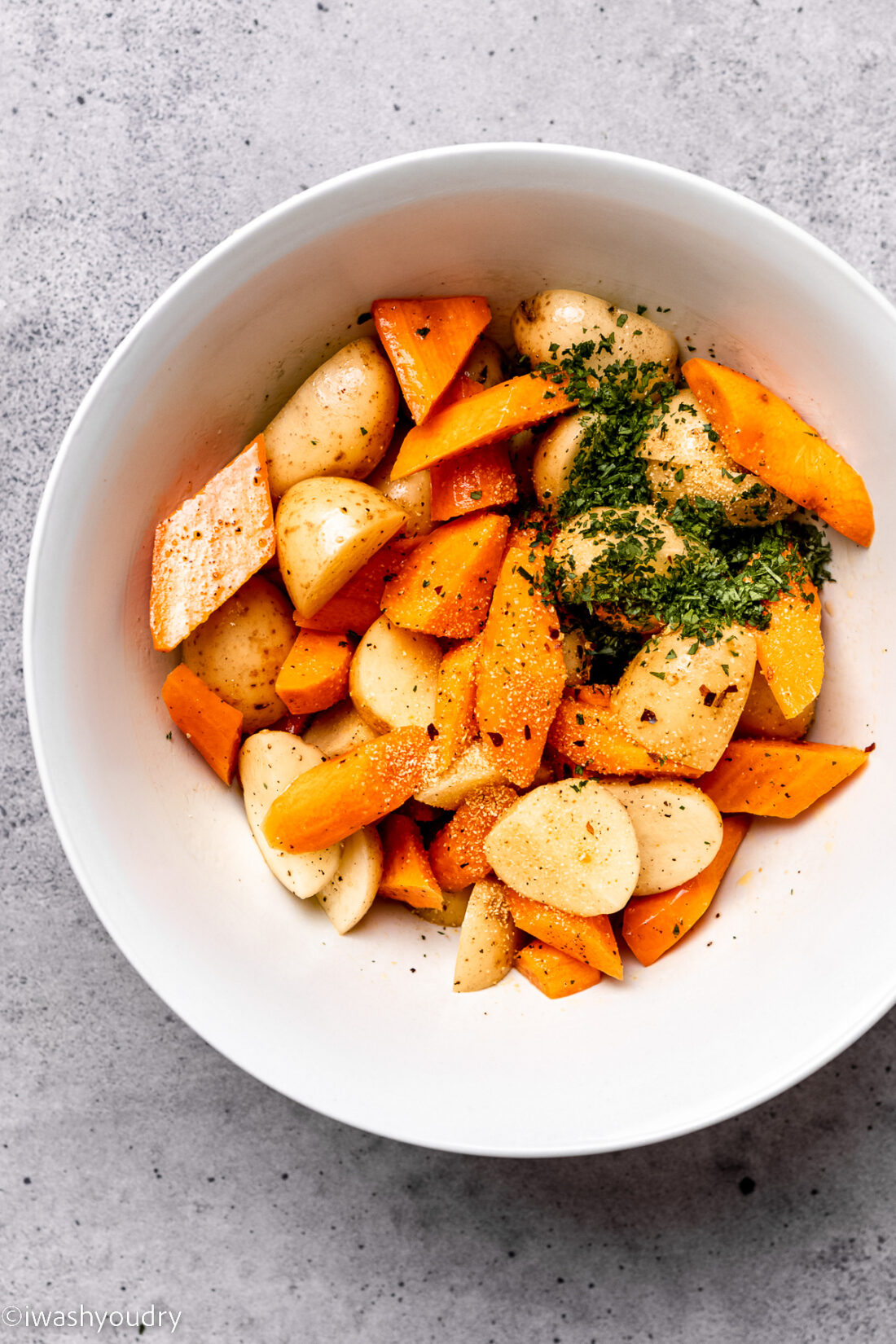 Herbs in bowl of raw chopped carrots and potatoes. 