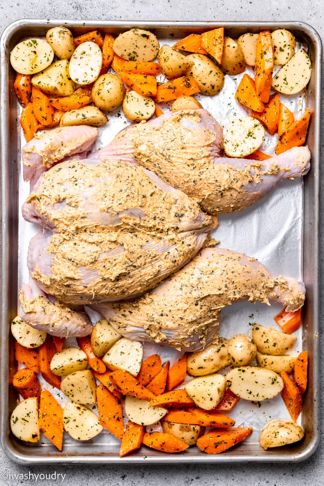 Raw Spatchcock chicken with vegetables on baking sheet.