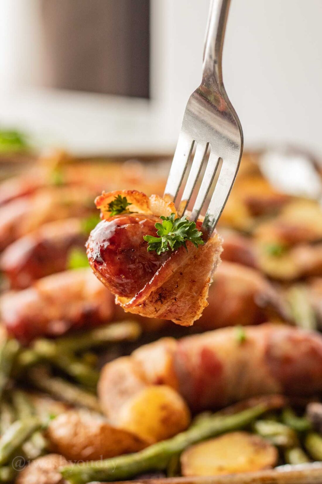 Bite of bacon wrapped bratwurst on a fork. 