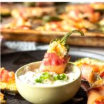 Bacon wrapped jalapeno popper in small bowl of sour cream.
