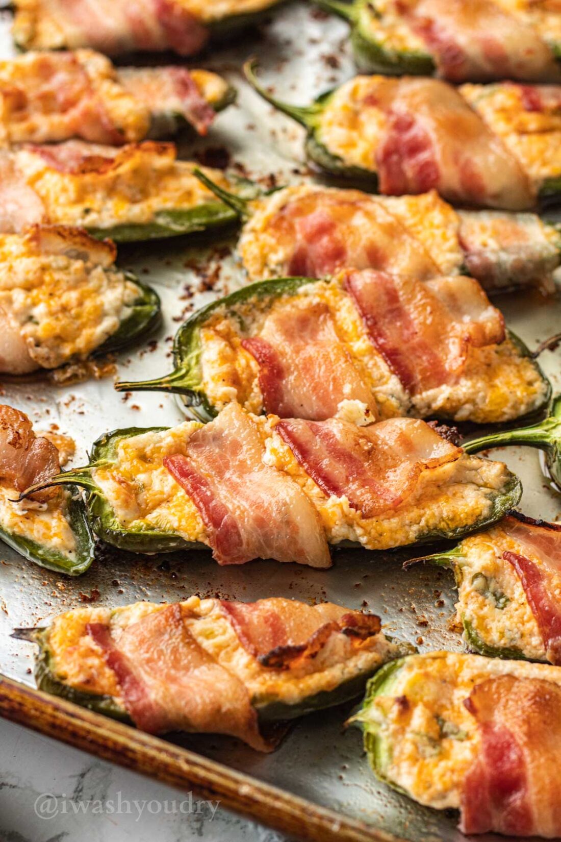 Cooked bacon wrapped Jalapeño Poppers on metal baking sheet. 