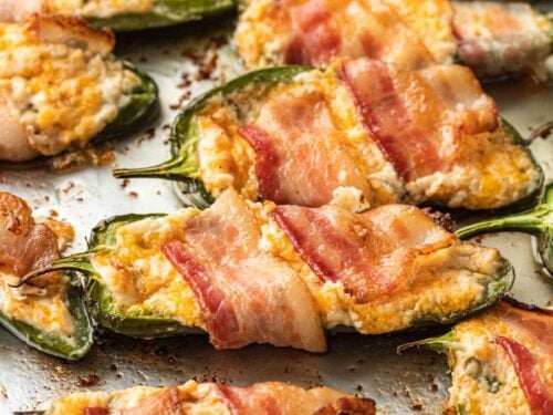 Cooked bacon wrapped Jalapeño Poppers on metal baking sheet.