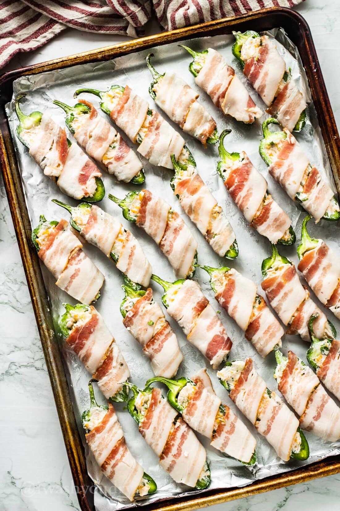 Raw bacon wrapped jalapeno poppers on metal baking sheet. 