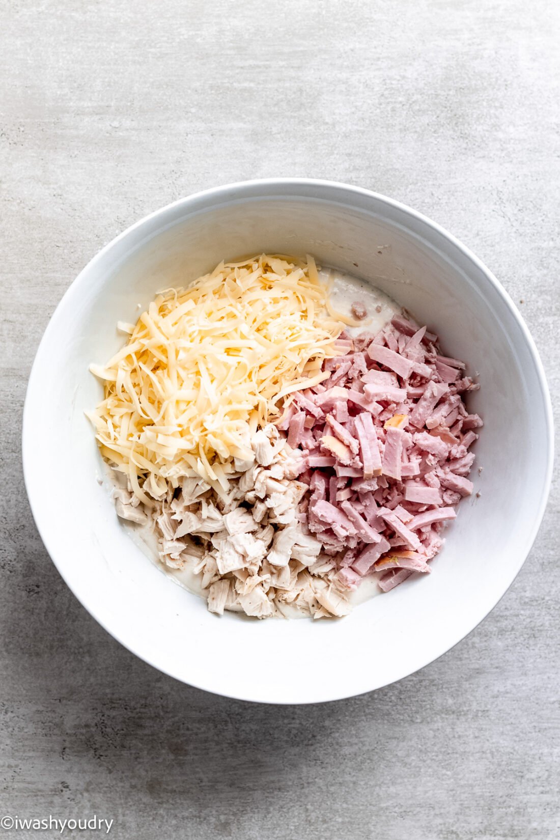 Ham, chicken, and cheese in a white bowl. 