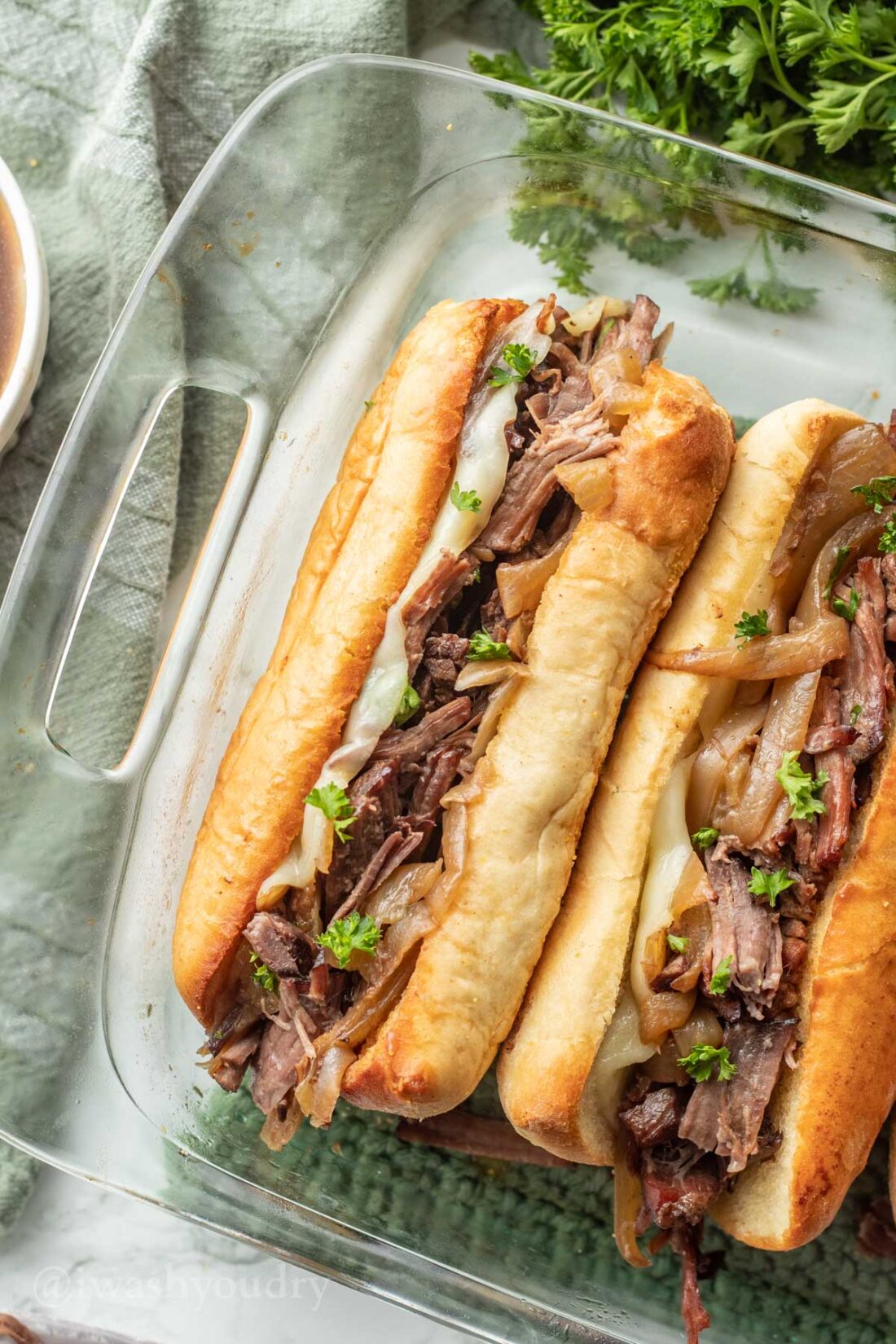 french dip sandwiches in casserole dish with cheese and sauce.