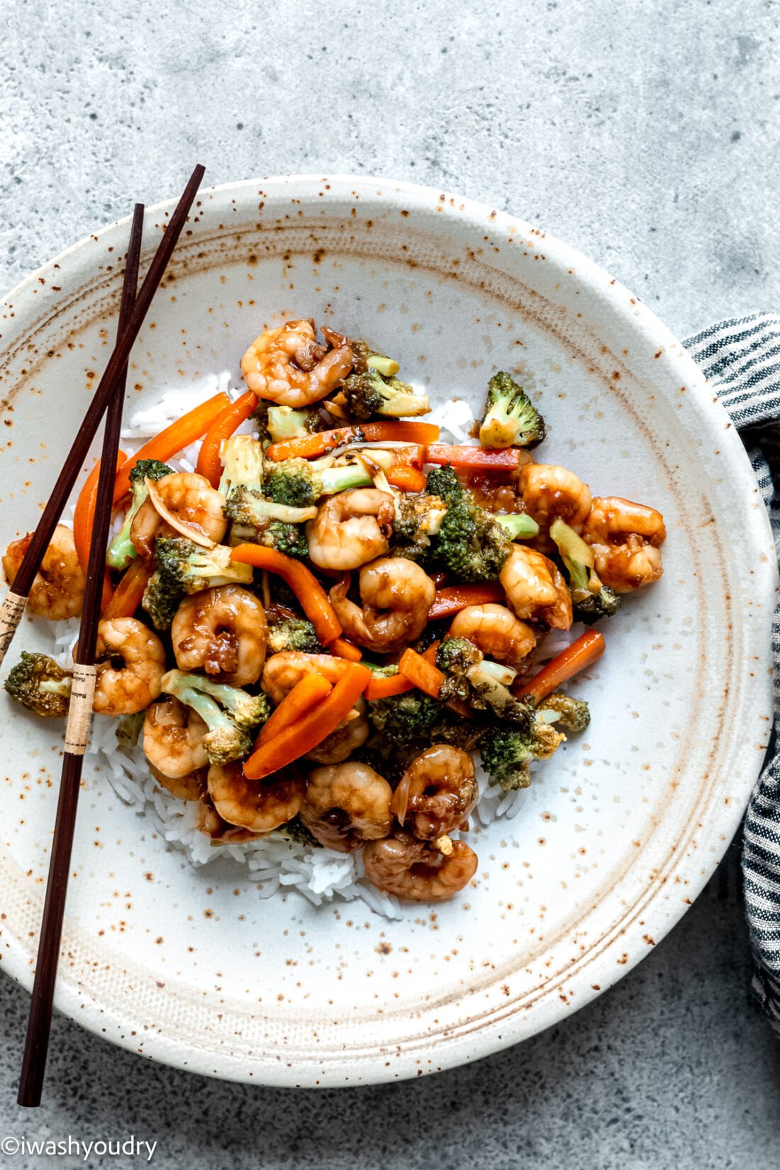 plate of shrimp with broccoli and carrots over white rice.