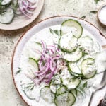 Sliced Cucumbers and red onions in a creamy dressing on a white plate.