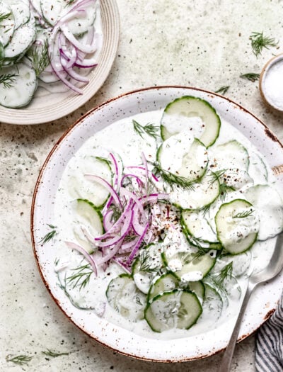 Sliced Cucumbers and red onions in a creamy dressing on a white plate.