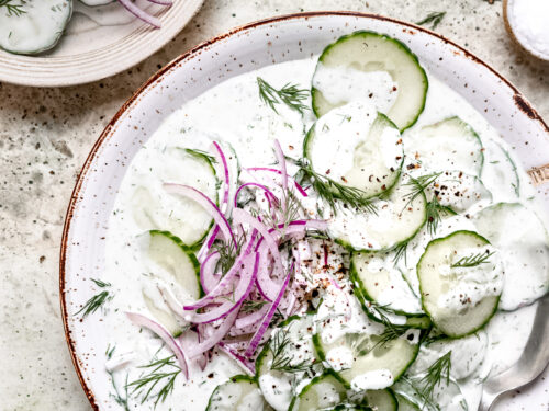 Sliced Cucumbers and red onions in a creamy dressing on a white plate.
