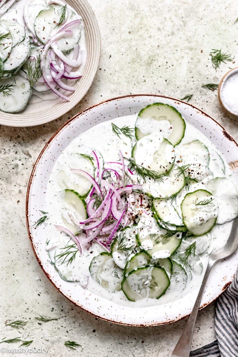 Sliced Cucumbers and red onions in a creamy dressing on a white plate.