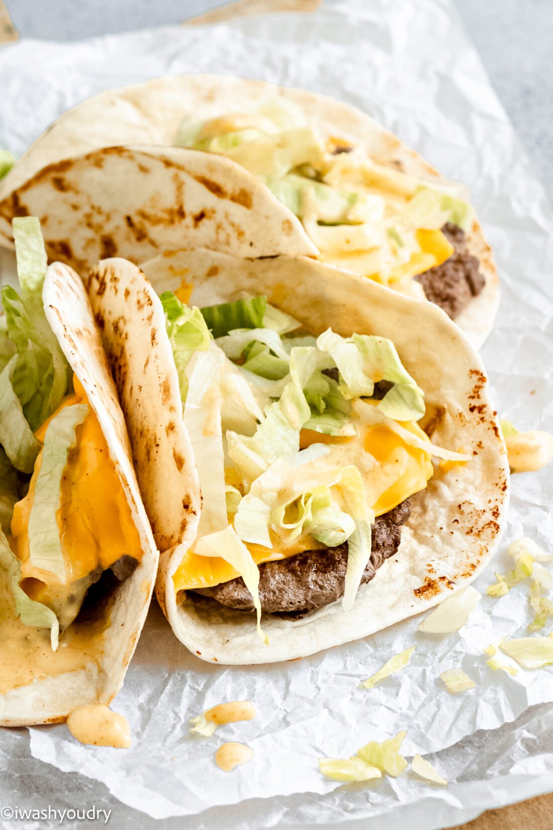 three small tacos with beef and cheese topped with lettuce and big mac sauce.