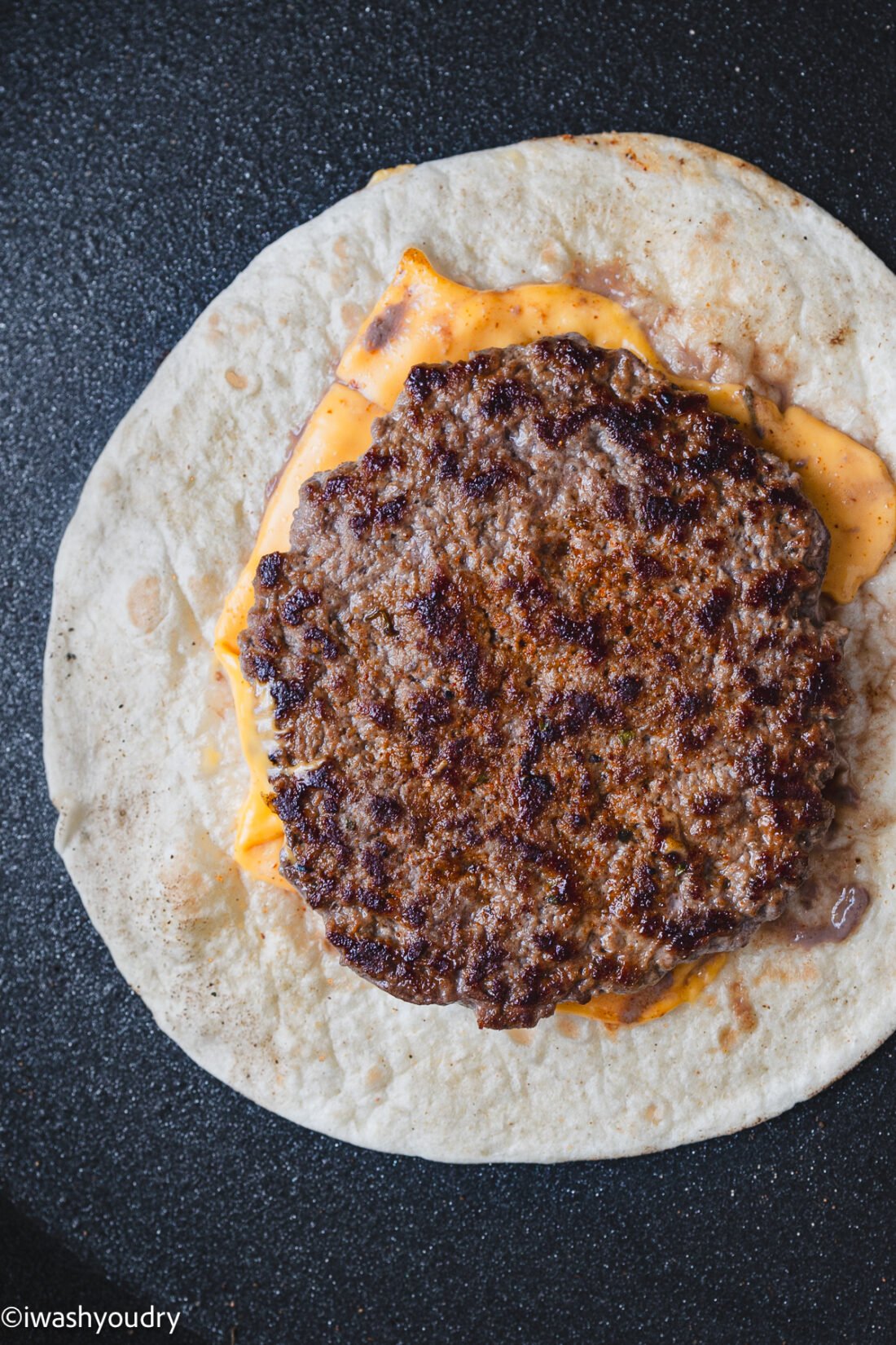 smashed burger on tortilla with cheese underneath.