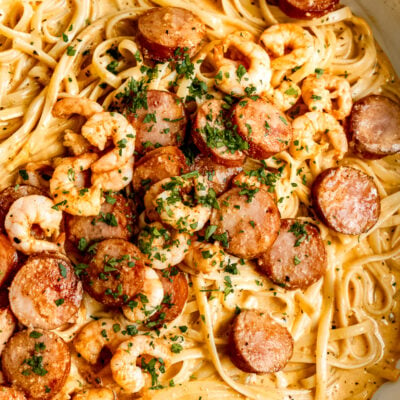 Cooked shrimp pasta with sausage and seasoning in metal pan.