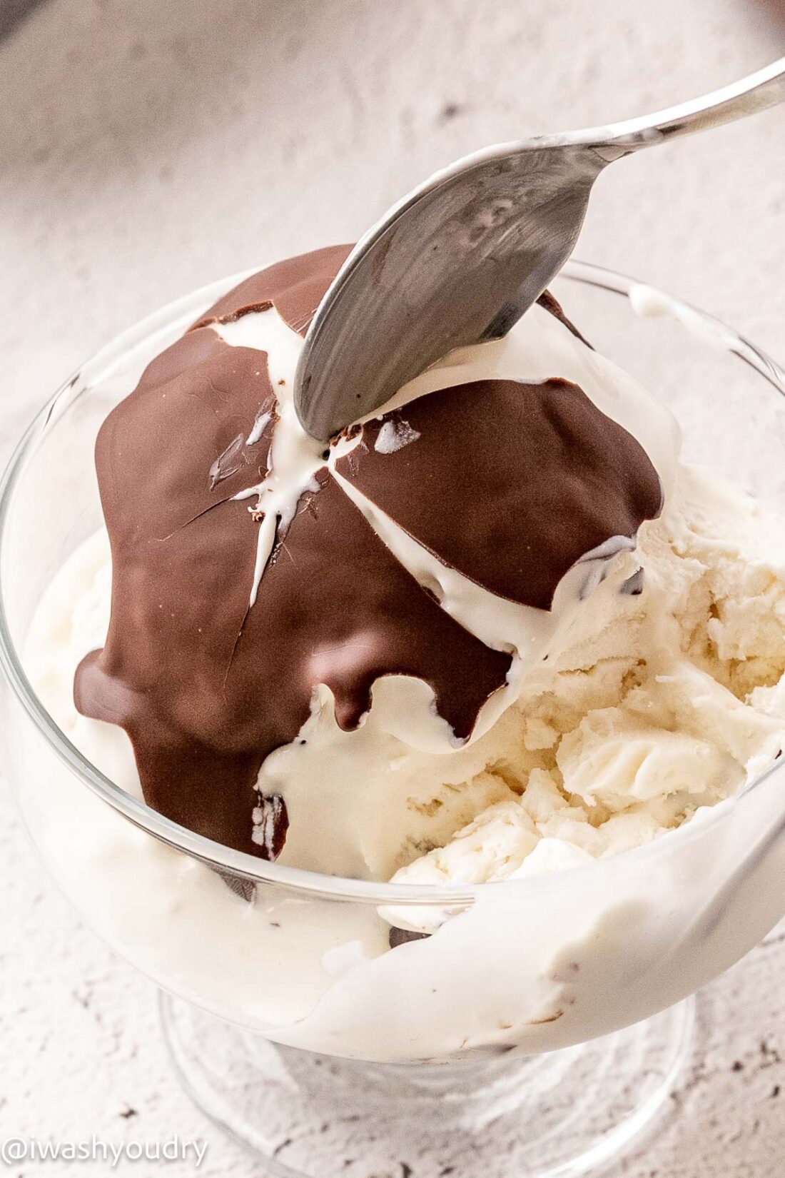 spoon breaking chocolate magic shell topping over vanilla ice cream.
