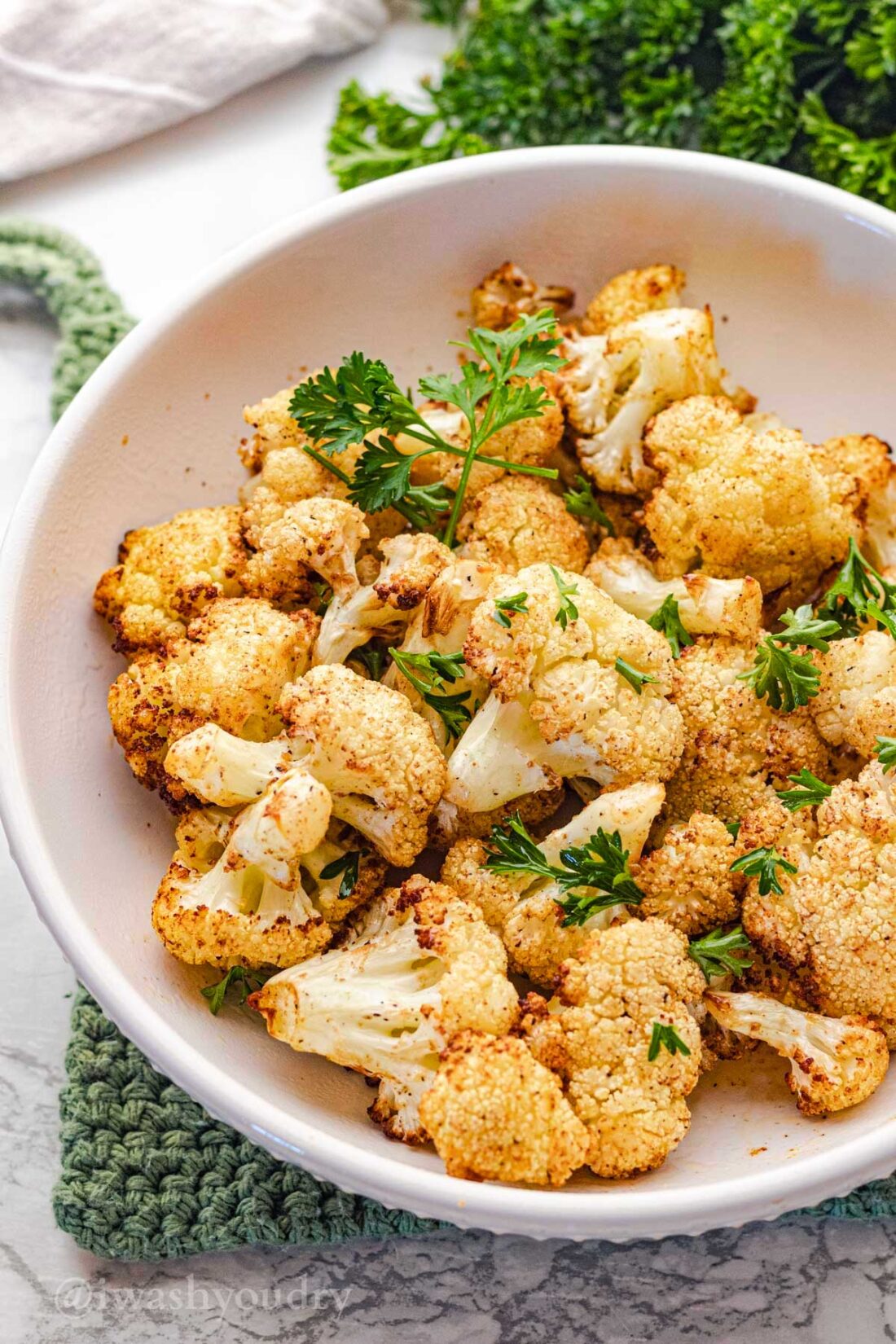 Cooked cauliflower with parsley in white bowl over green pot holder. 